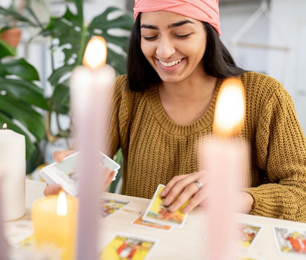 Happy indian woman reading tarot cards with candles at home. Hindu millennial female reading cards.